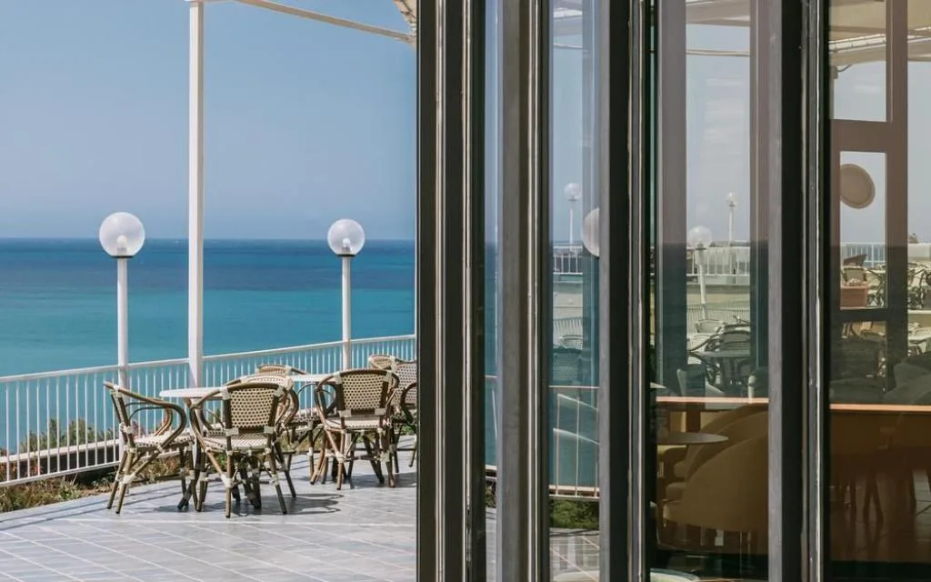 Terrazza con tavoli e sedie in vimini affacciata sul mare vista dall'interno