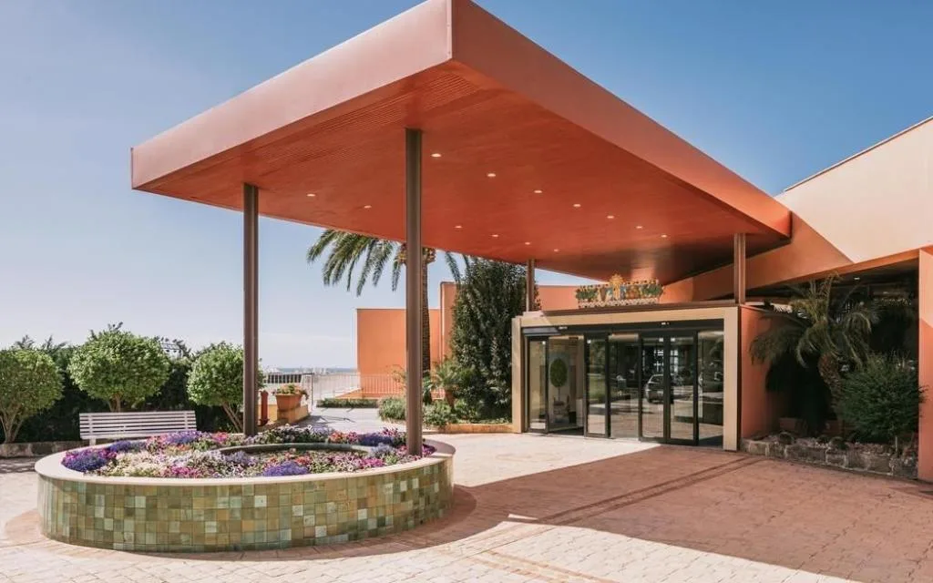 Ingresso dell'hotel con pensilina, aiuola fiorita e palme
