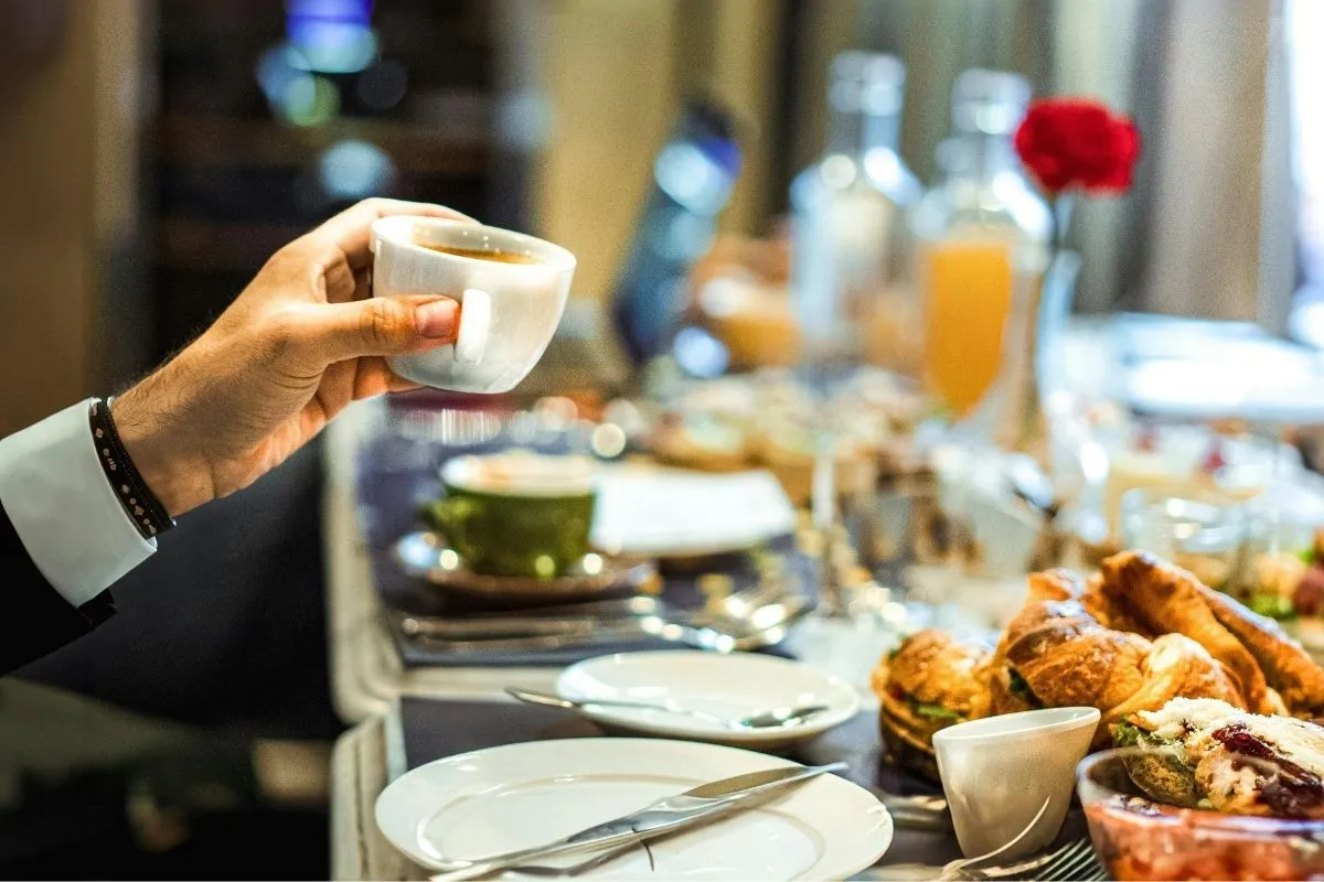 Colazione a buffet con caffè in mano, succhi e cornetti su tavolo elegante