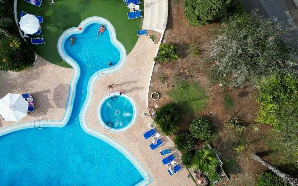 Vista aerea di piscina curva con idromassaggio, lettini blu e giardino