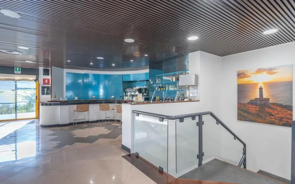 Area bar e hall con bancone azzurro, scala con ringhiera in vetro e quadro decorativo