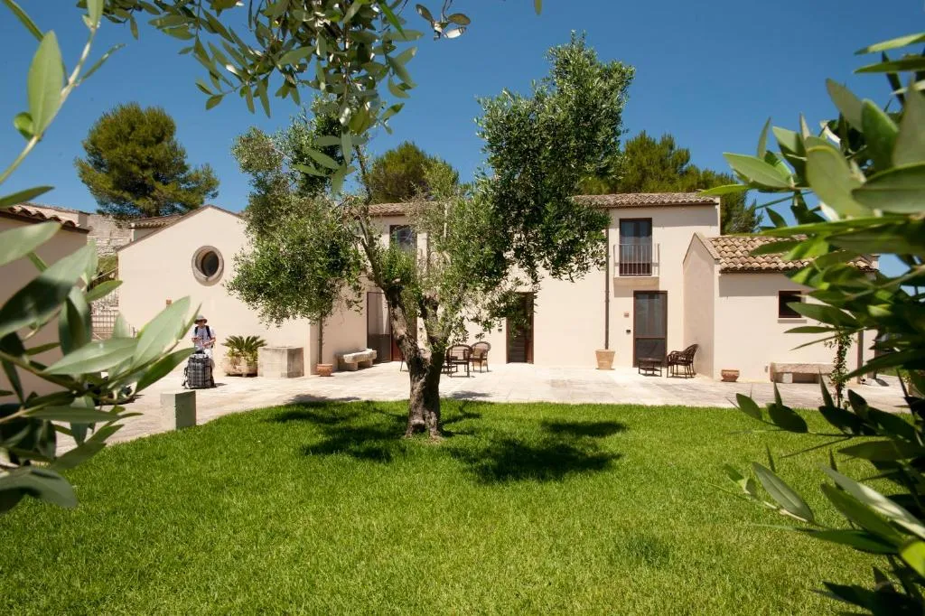 Cortile esterno della masseria con ulivo, prato verde e edificio in pietra chiara