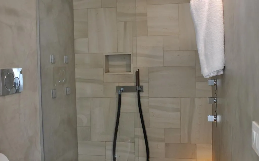 Doccia moderna con rivestimento in pietra chiara e asciugamano bianco