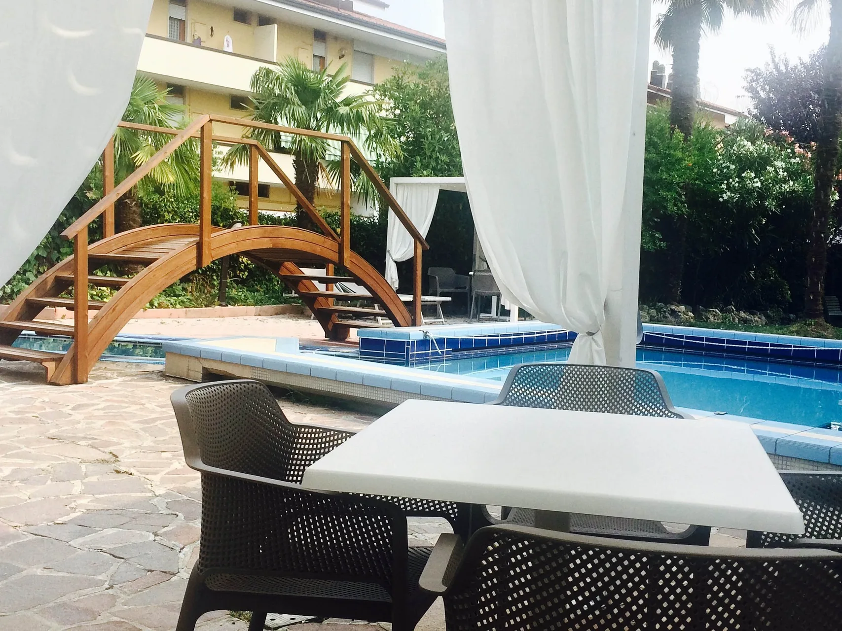 Area relax a bordo piscina con ponticello in legno, tavolo e sedie