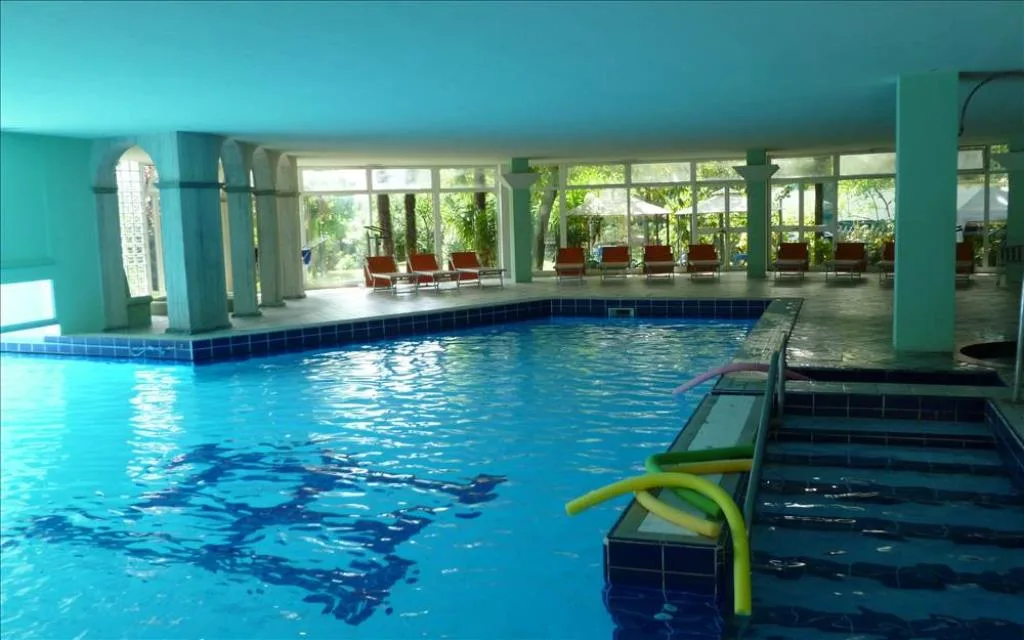 Piscina coperta con acqua azzurra, colonne e lettini vista giardino