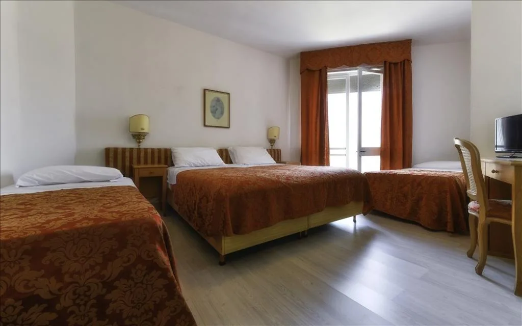 Camera tripla con letti coperte arancioni, scrivania e balcone