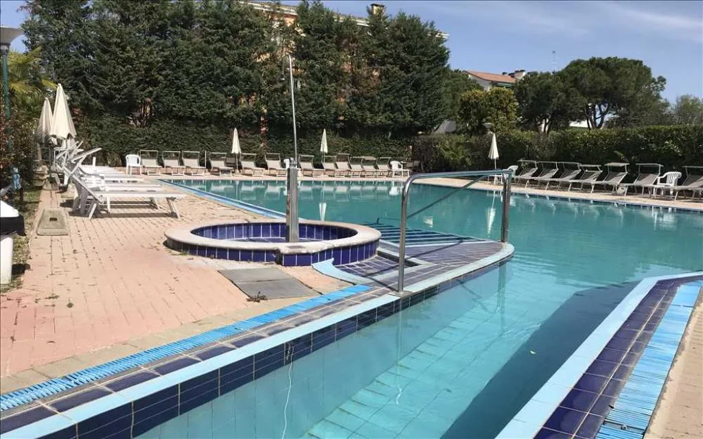 Piscina esterna con idromassaggio circondata da lettini e siepi verdi