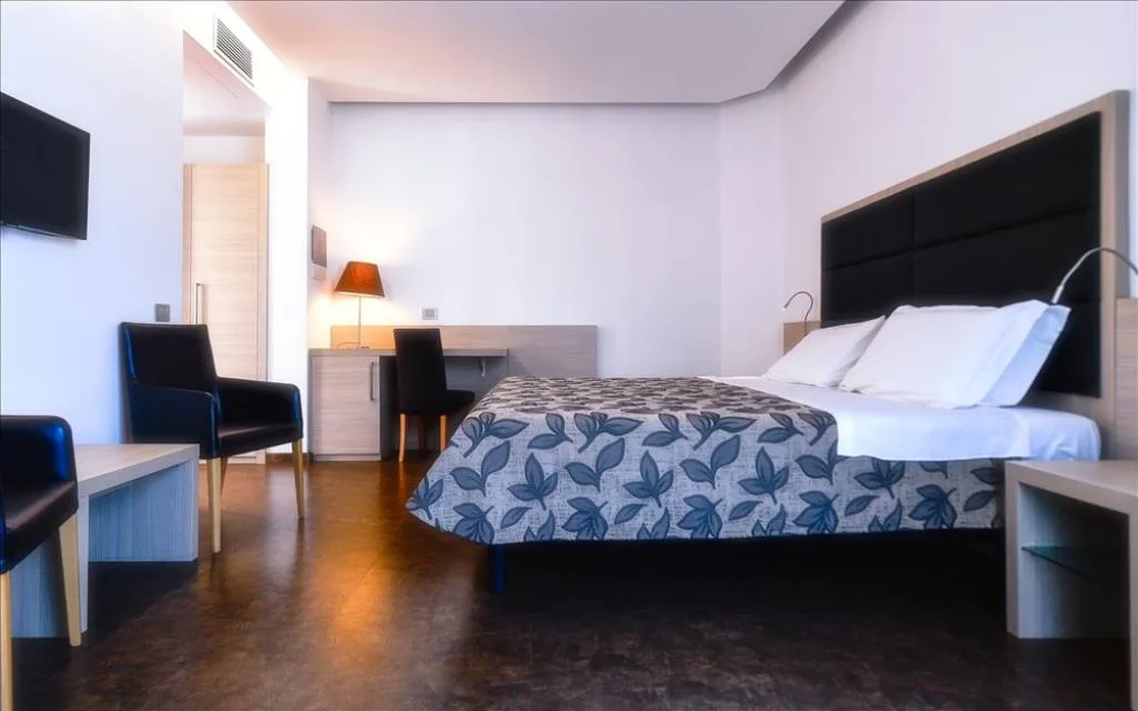 Camera moderna con letto matrimoniale, poltrone nere e TV a parete