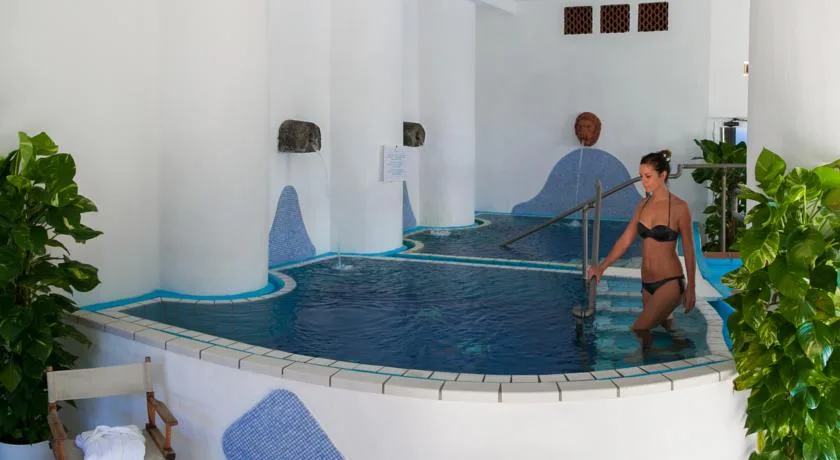 Piscina termale coperta con pareti bianche e dettagli a mosaico