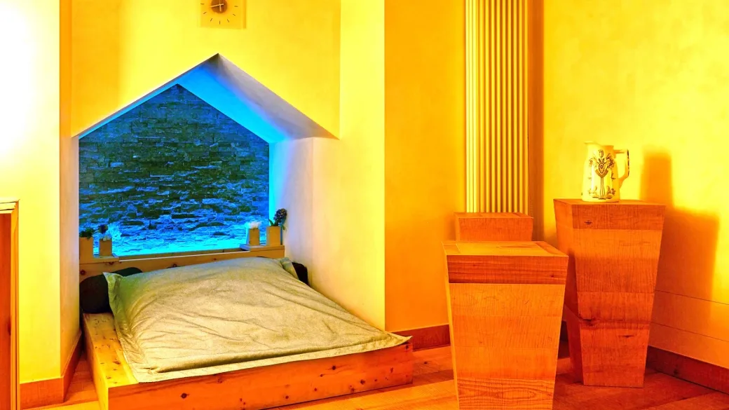 Camera con letto in legno e nicchia illuminata in pietra dai toni caldi
