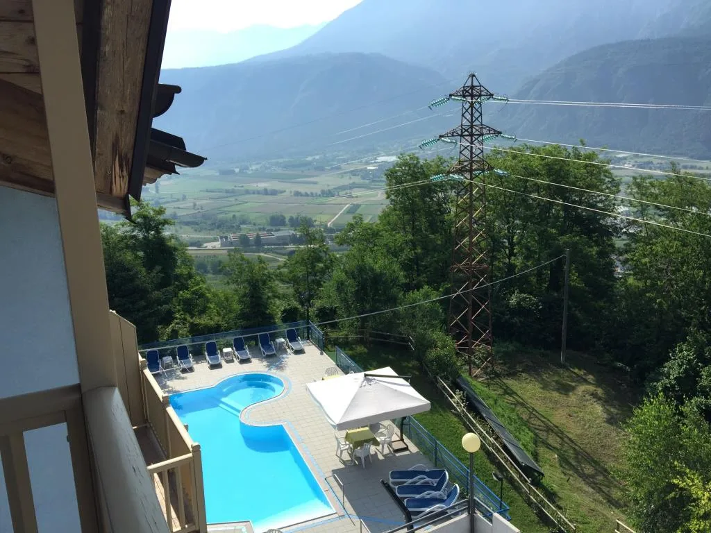 Vista dal balcone sulla piscina esterna con lettini e panorama montano