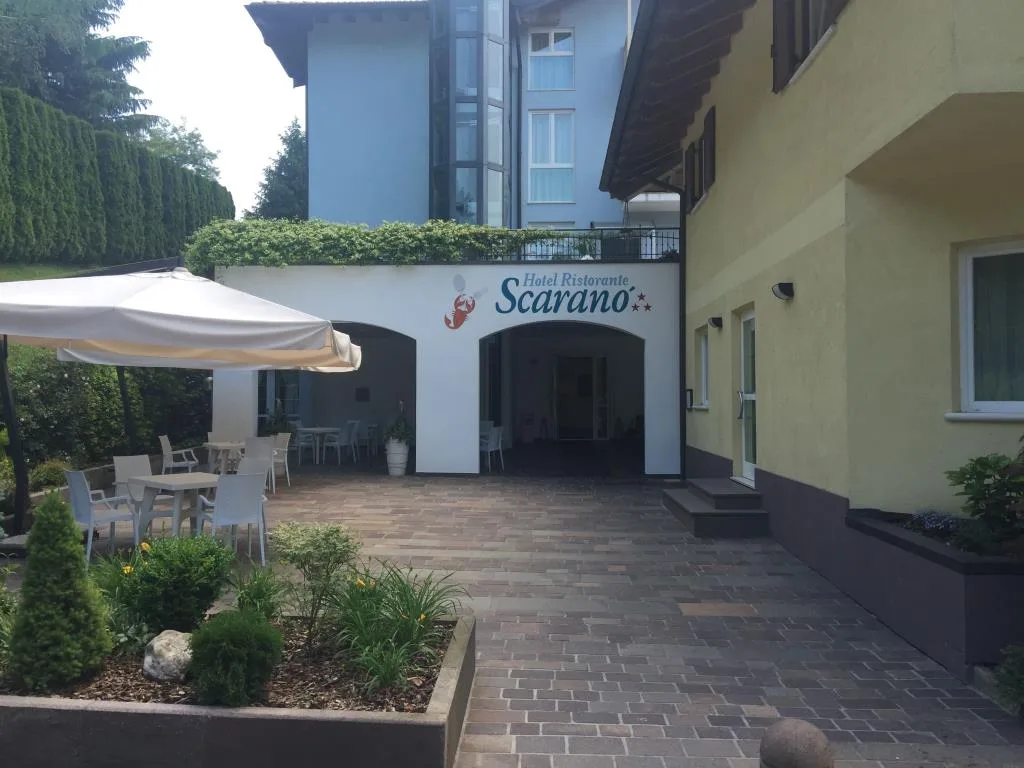 Cortile e ingresso dell'hotel con dehors coperto, tavoli e giardino con aiuole