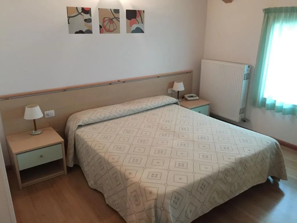Camera matrimoniale con letto, comodini, lampade e termosifone accanto alla finestra