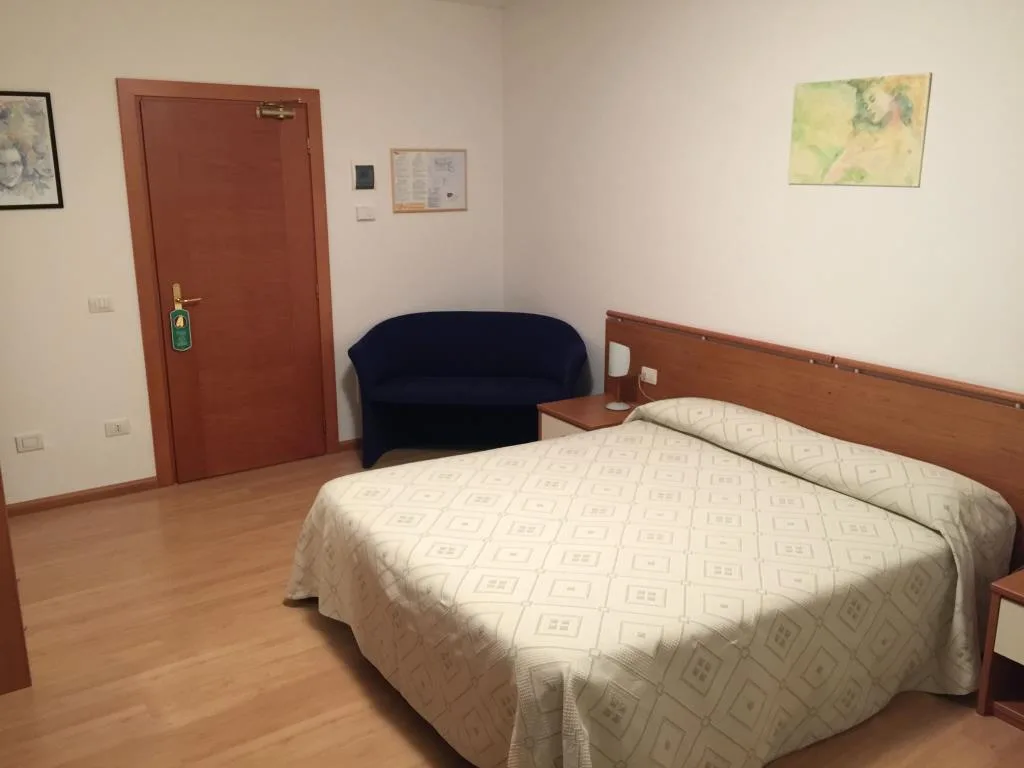 Camera con letto matrimoniale, divanetto blu e porta d'ingresso in legno