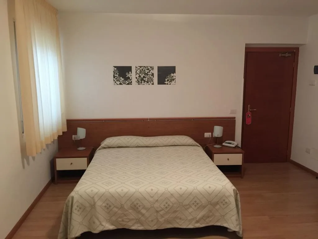 Camera matrimoniale luminosa con comodini in legno, tende chiare e decorazioni a parete