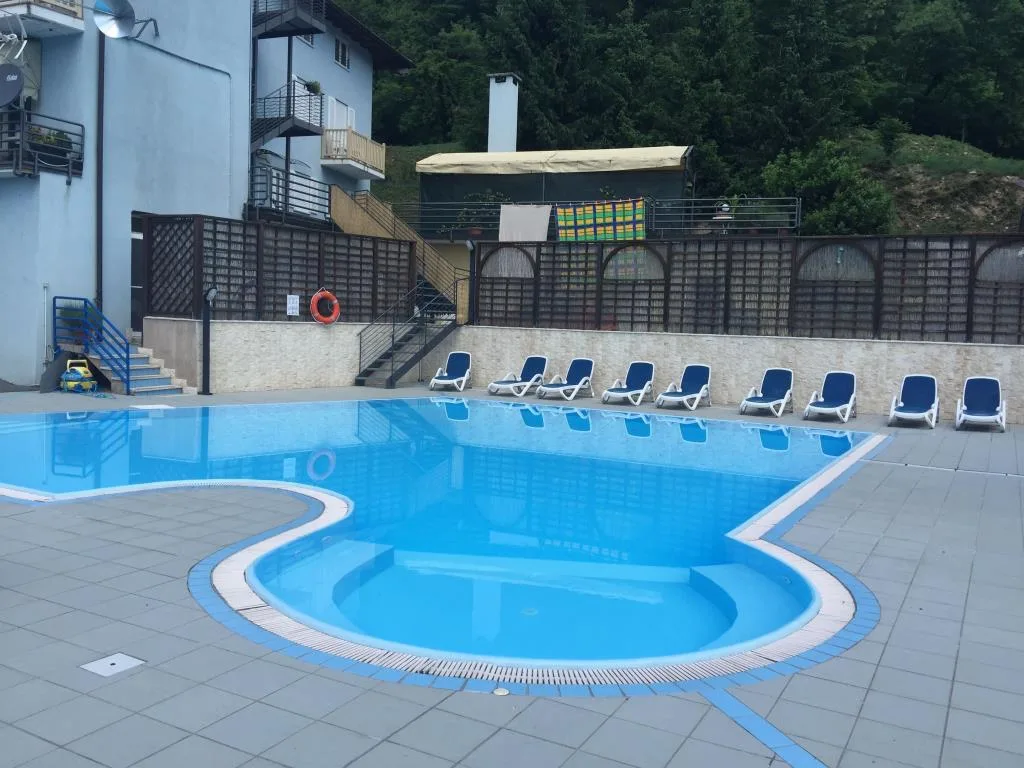 Piscina esterna con lettini blu, area solarium e recinzione in legno