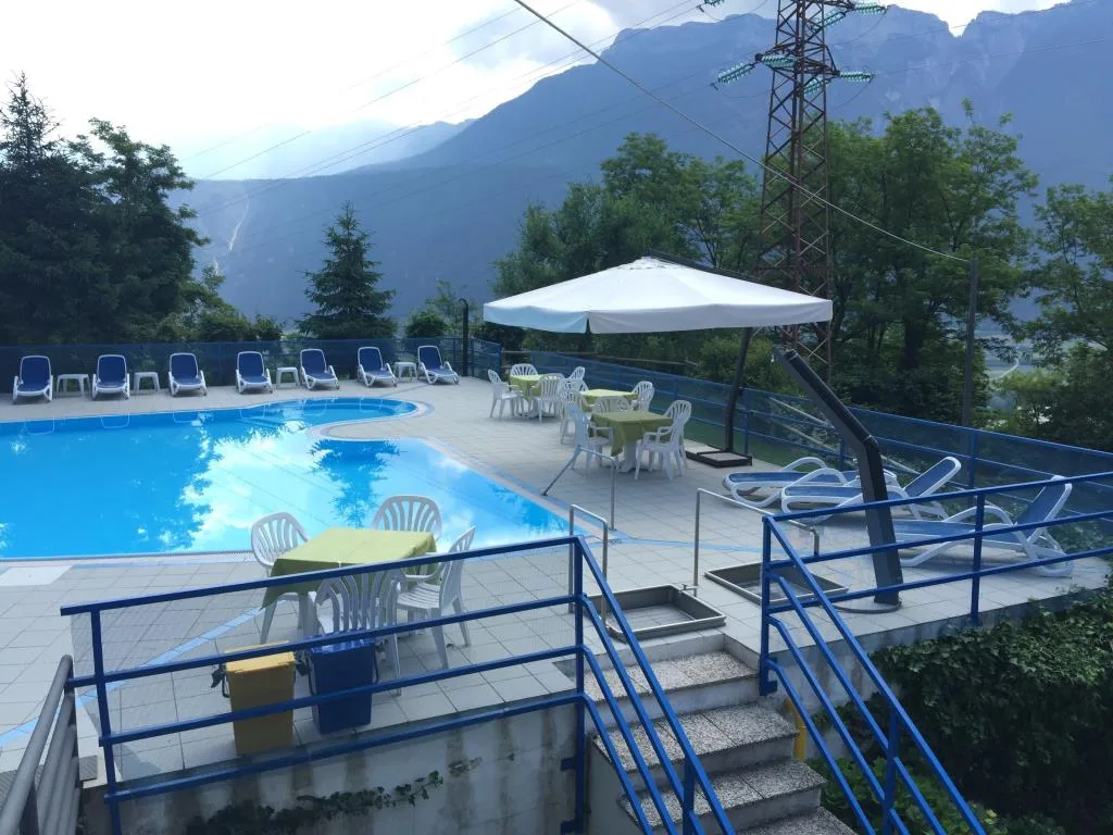 Terrazza con piscina, ombrellone bianco, tavoli e vista sulle montagne