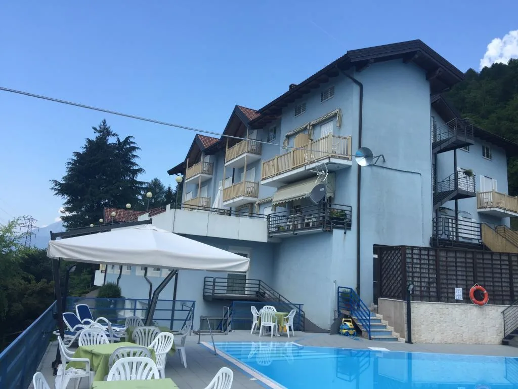 Piscina esterna con area relax, tavoli e ombrellone accanto all'edificio dell'hotel