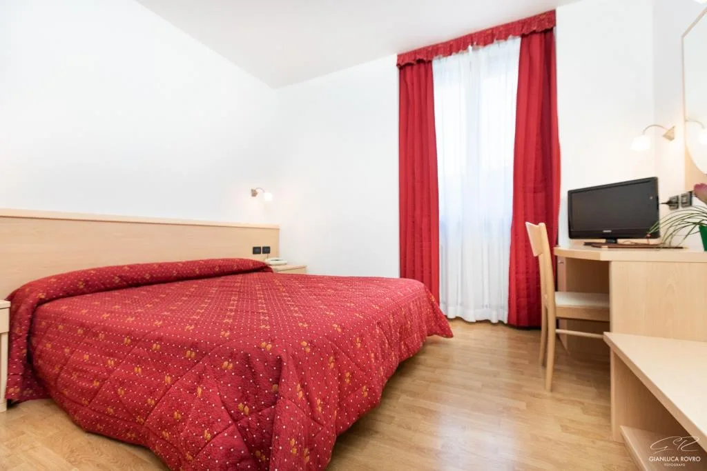 Camera matrimoniale con copriletto rosso, tende rosse e scrivania