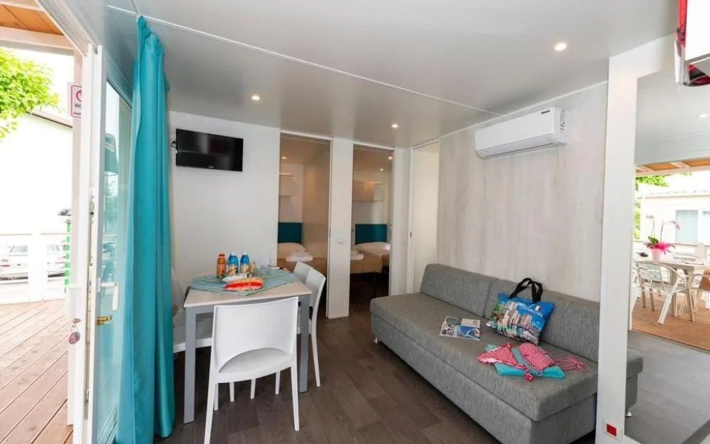 Interno luminoso di mobile home con soggiorno, divano, angolo pranzo e camera