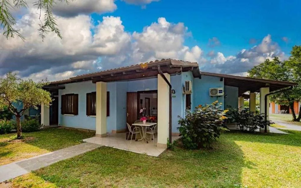 Villetta azzurra con veranda, tavolo e giardino curato sotto cielo azzurro