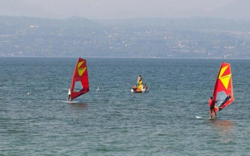 Windsurf e attività acquatiche sul lago con colline sullo sfondo