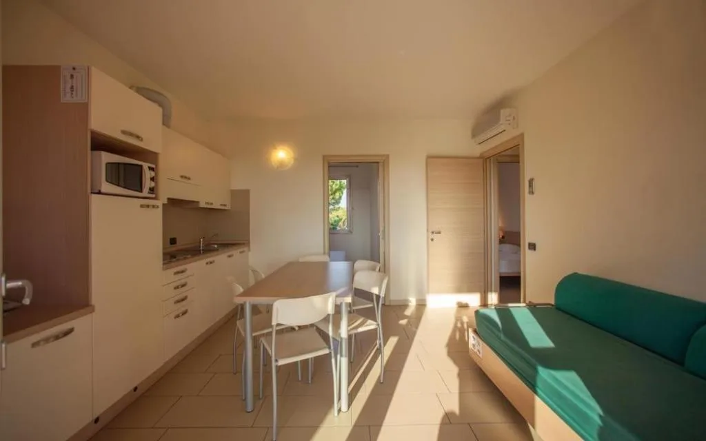 Soggiorno luminoso di appartamento con cucina, tavolo da pranzo e divano verde