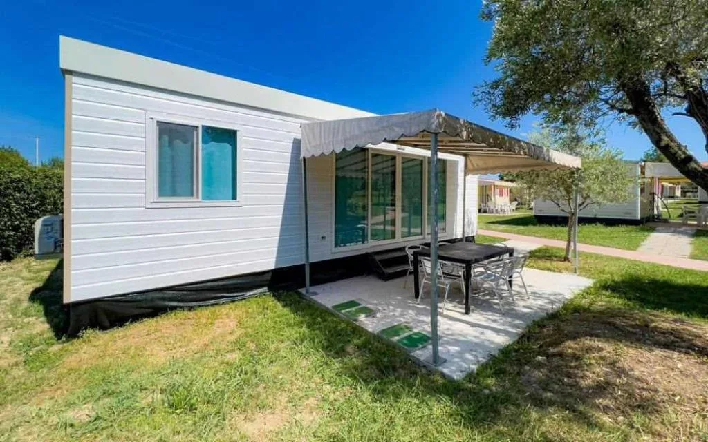 Mobile home moderna bianca con veranda, tavolo e ombrellone nel giardino